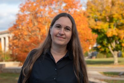 A photo of Naomi Creer featuring an Autumn backdrop, highlighted by orange Fall foliage.