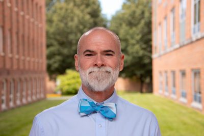 A photo of Assistant Professor Mark Dietrich between the Library and Administrative Building.