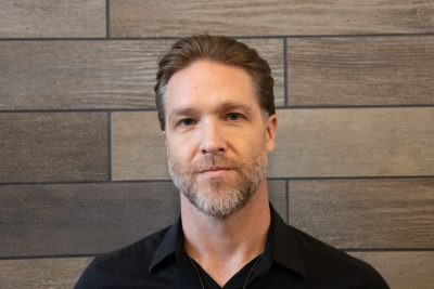 A photo of Jesse Yuhasz standing in front of a slate tile wall.