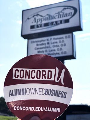 A Concord University Alumni Owned Business Sticker being held in from of the Appalachian Eye Care sign