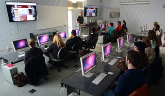 A group of students working in the graphic design lab while Professor Kevin Bennington gives a lecture