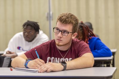 Three students writing and listening during a class