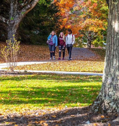 A group of three students walking around Concord University's campus. The trees have orange leaves and it is sunny