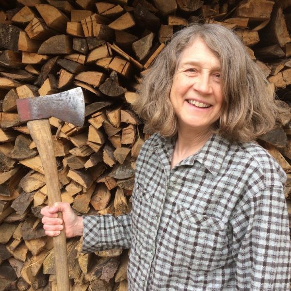 A photo of Linda Christianson, the guest artist for the 2024 WV Potters' Gathering, holding an axe in front of a large pile of wood