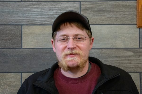 A photo of Cecil Williams standing in front of a gray slate tile wall.