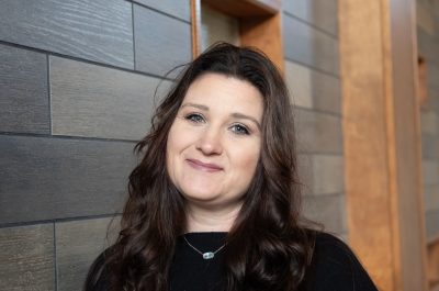 A photo of Jessica Doty Lilly, GEAR UP SWV Communications Manager and Cheerleading Coach, in front of a gray brick wall