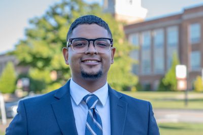 A photo of Joanthony Hernandez, one of our International Admissions Counselors, with the Concord campus greenery in the background.