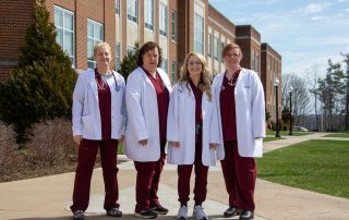 Department of Nursing Faculty stand together in front of Marsh Hall on Concord University's main campus. Faculty members include (from left to right) Professor Danita Farley, Dr. Martha Snider, Professor Amanda Nichols, and Dr. Michele Holt.