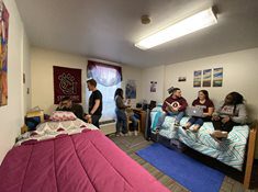 Students inside of a room in the Towers residence halls. The room has two beds, a window, two desks, and lots of posters